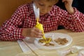 Boy in a plaid shirt is decorating the cookies in the shape of an angel with yellow cream