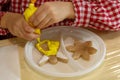 Boy in a plaid shirt is decorating with yellow cream the cookies in the shape of an angel and a star