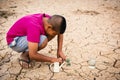 Boy planting little green tree on crack dry ground