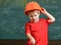 Boy play as builder or architect. Kid boy in orange hard hat or helmet, chalkboard on background. Child dreaming about