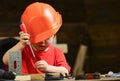 Boy play as builder or repairer, work with tools. Childhood concept. Kid boy in orange hard hat or helmet, study room