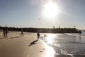 Boy playing ball at the beach while other people stroll by or fish or climb the rocks in late afternoon - silhouettes and lens fla