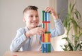 Boy is playing with colored wooden bricks by building tower. Motor skills improvement