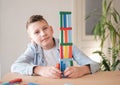 Boy is playing with colored wooden bricks by building tower. Motor skills improvement