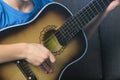 Boy is playing guitar sitting on the couch, hands close-up. Concept of learning to play a musical instrument. Royalty Free Stock Photo