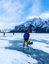 Boy enjoys ice hockey on frozen Lake Minnewanka, or Minn-waki (Lake of Spirits), surrounded spectacular mountains.