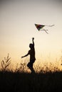 Boy playing kite on summer sunset meadow silhouetted Royalty Free Stock Photo