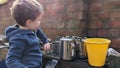 A boy playing with a mud outdoor kitchen holding utensils