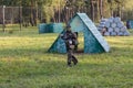 Boy is playing paintball on the field. two teams of paintball players in camouflage form with masks, helmets, guns on the field