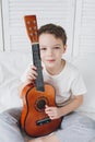 Boy playing a small guitar sitting on the bed Royalty Free Stock Photo