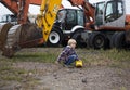 boy playing with a toy bulldozer in front of several real big wheeled excavators with huge metal buckets