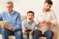 Boy Playing Videogame Sitting Between Grandfather And Father At Home
