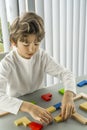 Boy playing with a wooden cube on the gray background. Multi-colored cubes on the table. Geometric shapes on a wooden Royalty Free Stock Photo