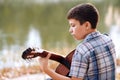 The boy plays an acoustic guitar, sits on the Bank of the river, autumn forest at sunset, beautiful nature and the reflection of t Royalty Free Stock Photo