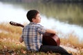 The boy plays an acoustic guitar, sits on the Bank of the river, autumn forest at sunset, beautiful nature and the reflection of t Royalty Free Stock Photo