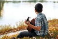 The boy plays an acoustic guitar, sits on the Bank of the river, autumn forest at sunset, beautiful nature and the reflection of t Royalty Free Stock Photo