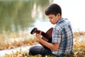 The boy plays an acoustic guitar, sits on the Bank of the river, autumn forest at sunset, beautiful nature and the reflection of t Royalty Free Stock Photo