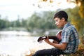 The boy plays an acoustic guitar, sits on the Bank of the river, autumn forest at sunset, beautiful nature and the reflection of t Royalty Free Stock Photo