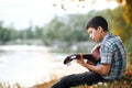 The boy plays an acoustic guitar, sits on the Bank of the river, autumn forest at sunset, beautiful nature and the reflection of t Royalty Free Stock Photo