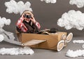 The boy plays in an airplane made of cardboard box and dreams of becoming a pilot, clouds of cotton wool on a gray background Royalty Free Stock Photo