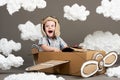 The boy plays in an airplane made of cardboard box and dreams of becoming a pilot, clouds from cotton wool on a gray background, r