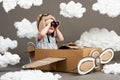 The boy plays in an airplane made of cardboard box and dreams of becoming a pilot, clouds from cotton wool on a gray background, r Royalty Free Stock Photo