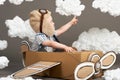 The boy plays in an airplane made of cardboard box and dreams of becoming a pilot, clouds from cotton wool on a gray background, r Royalty Free Stock Photo