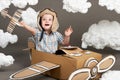 The boy plays in an airplane made of cardboard box and dreams of becoming a pilot, clouds from cotton wool on a gray background, r Royalty Free Stock Photo