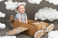 The boy plays in an airplane made of cardboard box and dreams of becoming a pilot, clouds from cotton wool on a gray background, r Royalty Free Stock Photo