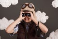 A boy plays with binoculars and dreams of becoming a pilot, dressed in a retro style jacket and helmet with glasses, clouds of