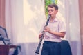 The boy plays the clarinet near the black piano by the window. Musicology, music education and education. Royalty Free Stock Photo