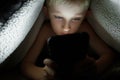 Boy plays games on a smartphone at night under a blanket on the floor Royalty Free Stock Photo