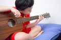 The boy plays the guitar with his left hand, a song by himself, on the sofa, in the bedroom, reading the sheet music Royalty Free Stock Photo