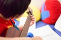 The boy plays the guitar with his left hand, a song by himself, on the sofa, in the bedroom, reading the sheet music. with capo Royalty Free Stock Photo