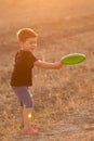 The boy plays the outdoors, throws a green frisbee disc, in the evening illumination Royalty Free Stock Photo