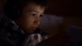 Boy plays on the Tablet lying in the dark in headphones