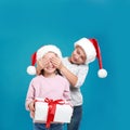 Boy presenting Christmas gift to girl on light blue background