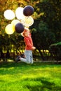 A boy of primary school age runs and jumps with balloons in an autumn sunny park. A red-haired boy with a bunch of multicolored