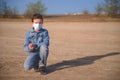 Boy in protective medical mask is sitting on the ground, upset and depressed Royalty Free Stock Photo