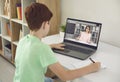 Boy pupil sitting at home and making notes during online lesson