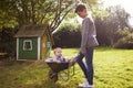 Boy Pushing Baby Brother In Garden Wheelbarrow