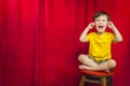 Boy Puts Fingers In Ears on Stool in Front of Theater Curtain Royalty Free Stock Photo