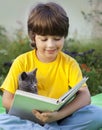 Boy reading book with kitten in the yard, child with pet reading magazine on the grass in park Royalty Free Stock Photo