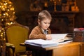 Boy reads a magic book while sitting at the table. Home interior with Christmas tree and fireplace. Traditional Royalty Free Stock Photo