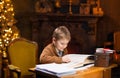Boy reads a magic book while sitting at the table. Home interior with Christmas tree and fireplace. Traditional
