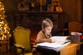 Boy reads a magic book while sitting at the table. Home interior with Christmas tree and fireplace. Traditional Royalty Free Stock Photo