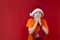 A boy on a red background in a Santa Claus hat holds a gift bag in his hands and is surprised Royalty Free Stock Photo