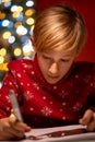 A boy in a red Christmas sweater on the background of a Christmas tree bent over the drawing in the process of decorating it with