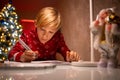 A boy in a red Christmas sweater on the background of a Christmas tree bent over the drawing in the process of decorating it with