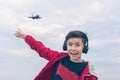 A boy in a red jacket and headphones smiling and shows his finger on the plane. Landing plane above sea waves in stormy weather Royalty Free Stock Photo